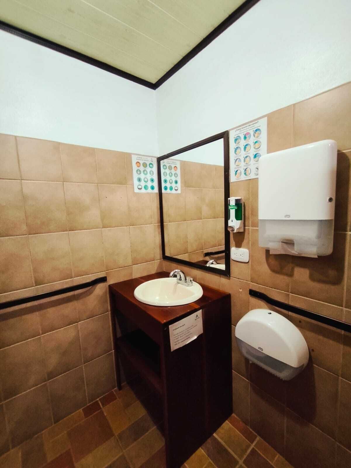 Baño con lavamanos, espejo, secador de manos y dispensador de toallas de papel.