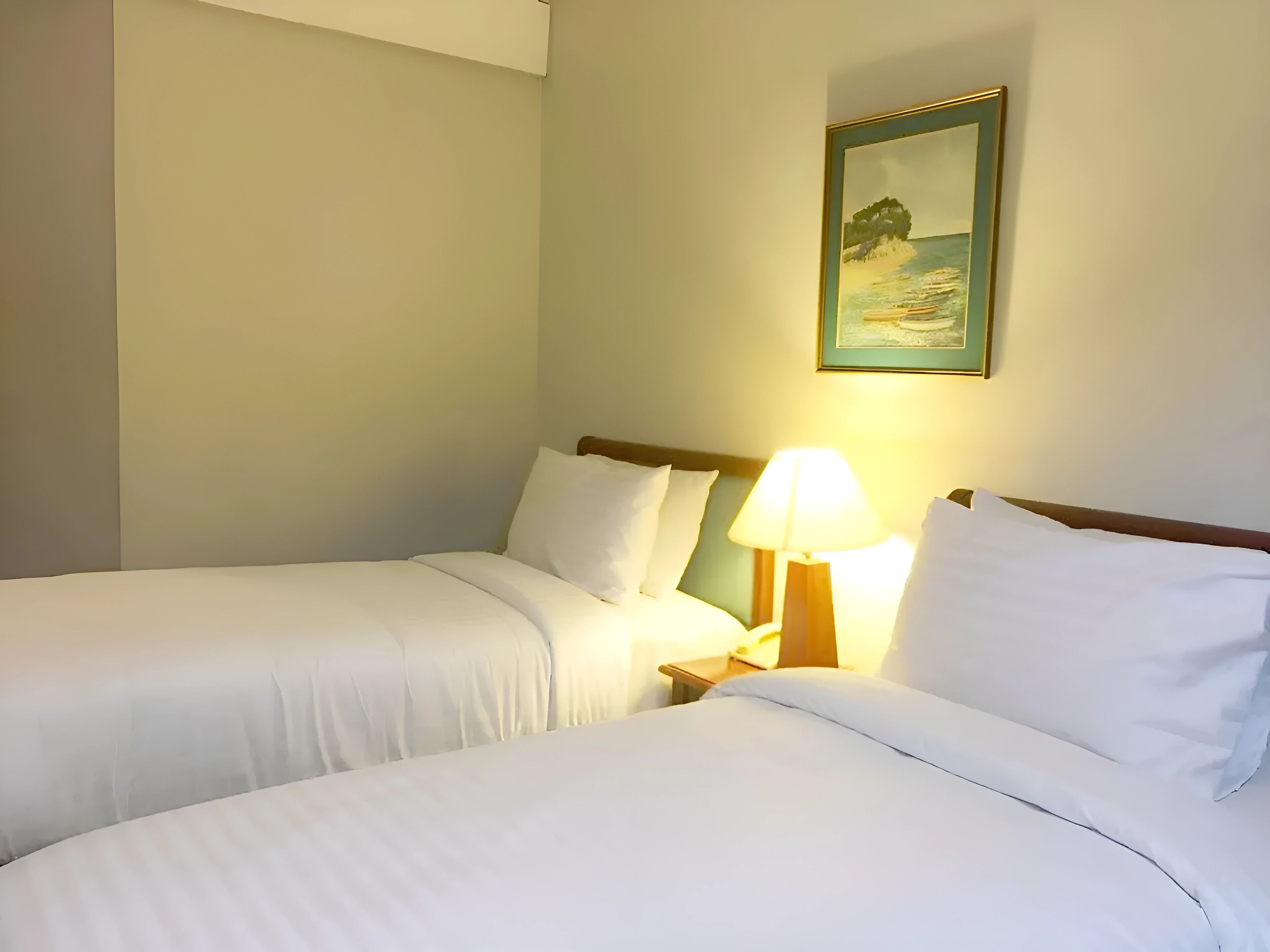 A hotel room with two single beds, a nightstand with a lamp, and a framed picture on the wall.