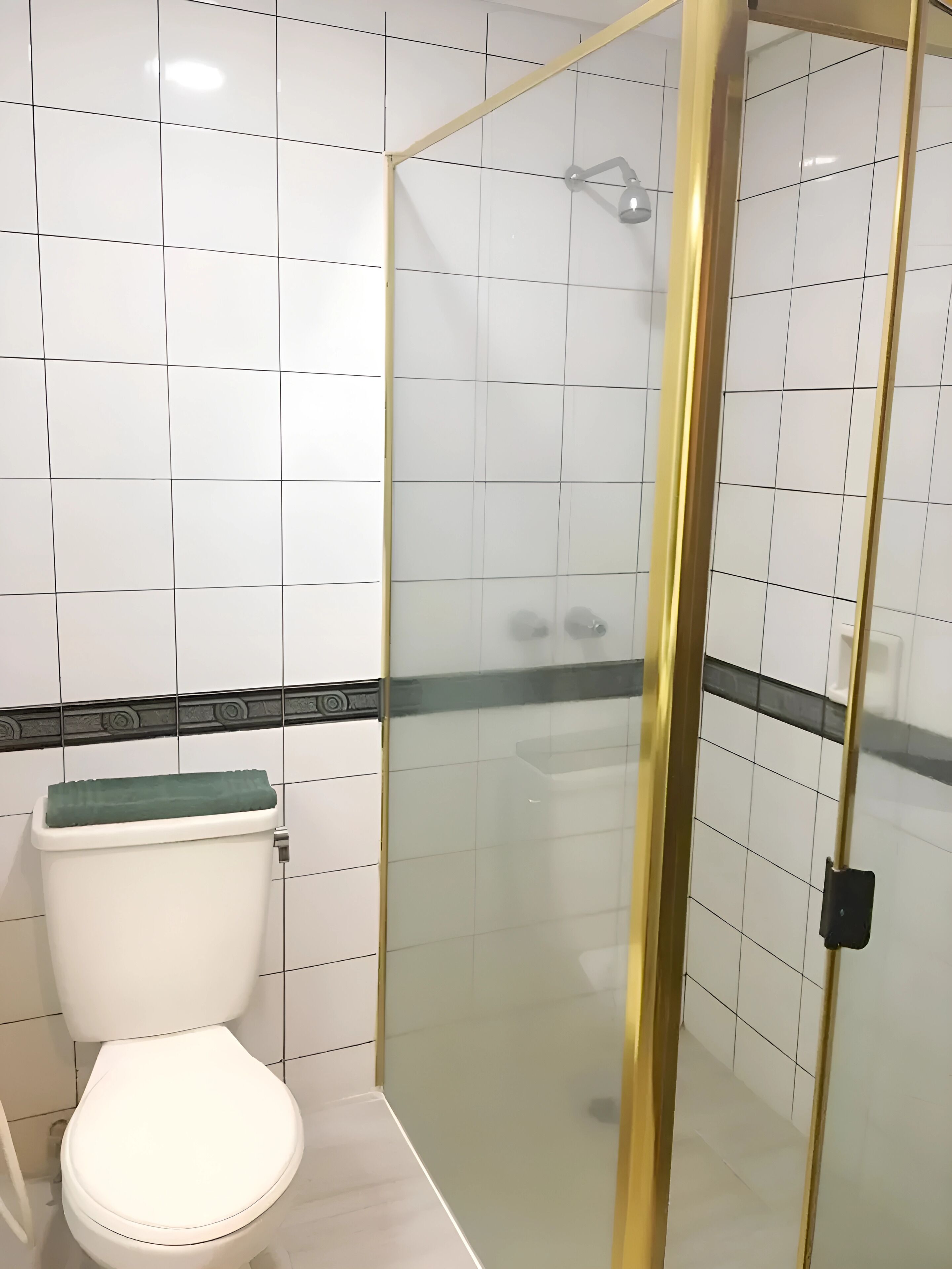 Een badkamer met toilet, douchecabine en witte betegelde wanden.