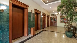 Un vestíbulo de hotel con puertas de madera, paredes de mármol y una planta en maceta.
