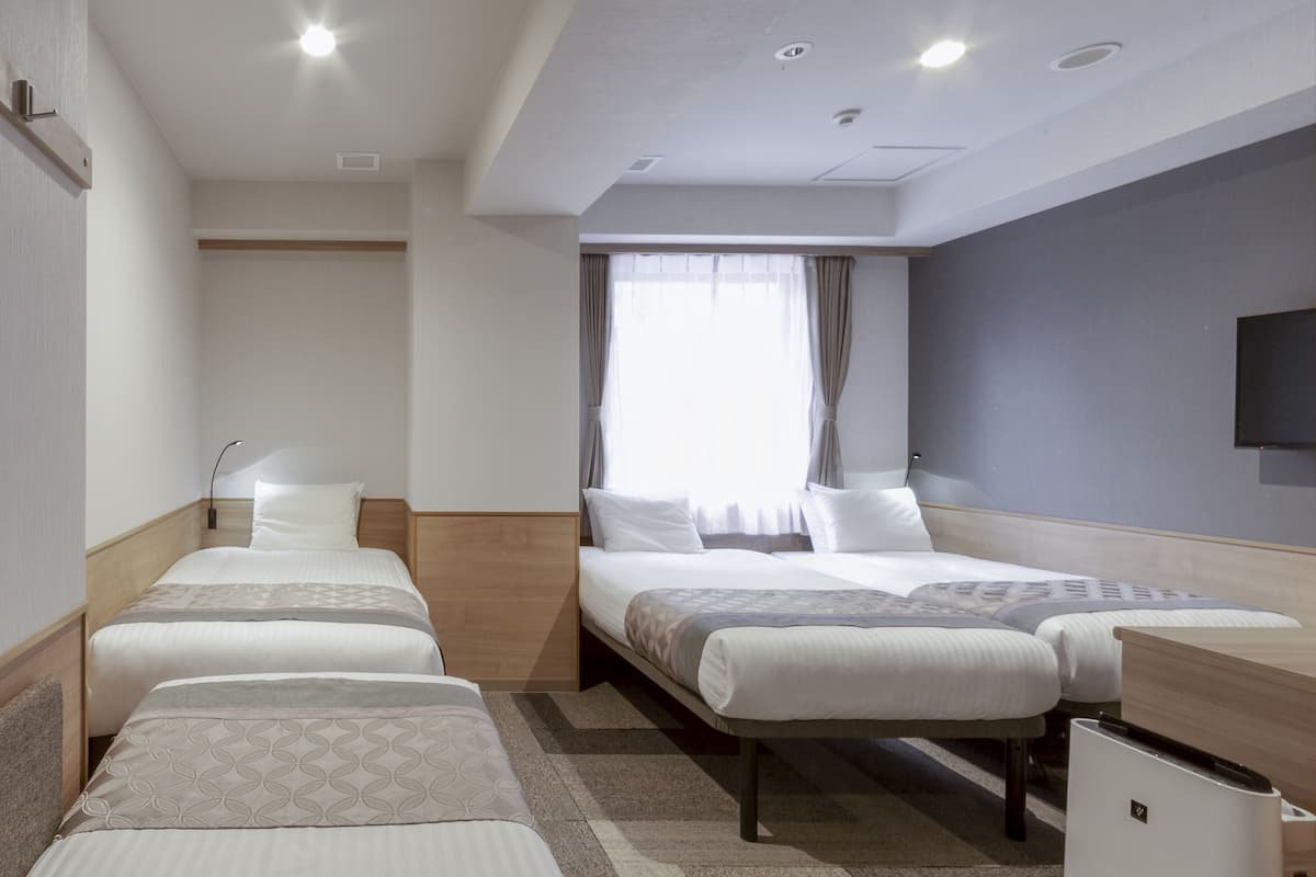 A hotel room with two beds, a desk, a TV, and a window with curtains.