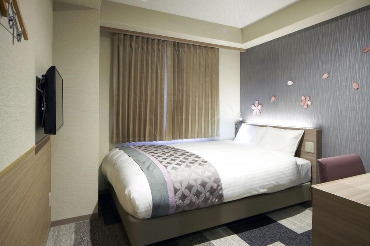 Une chambre d’hôtel avec un lit, un bureau, une télévision et une fenêtre avec des rideaux.