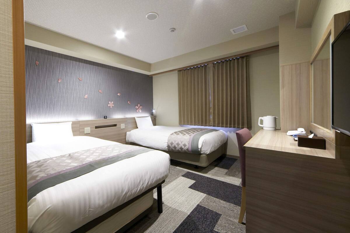 A hotel room with two beds, a desk with a coffee maker, a TV, and a window with curtains.