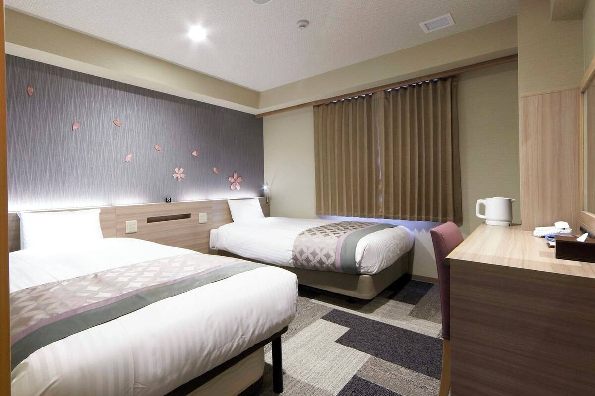 A hotel room with two beds, a desk, a TV, and a window with curtains.
