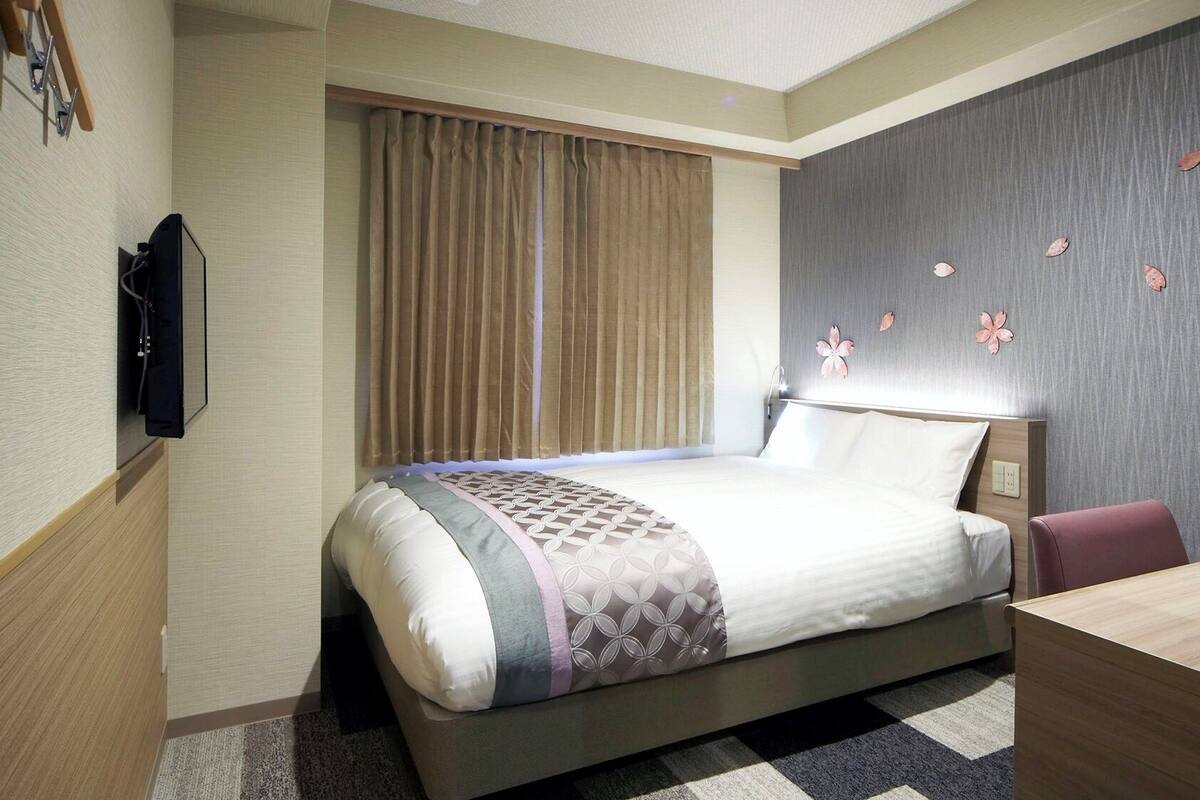 A hotel room with a bed, a desk, a television, and a window with curtains.