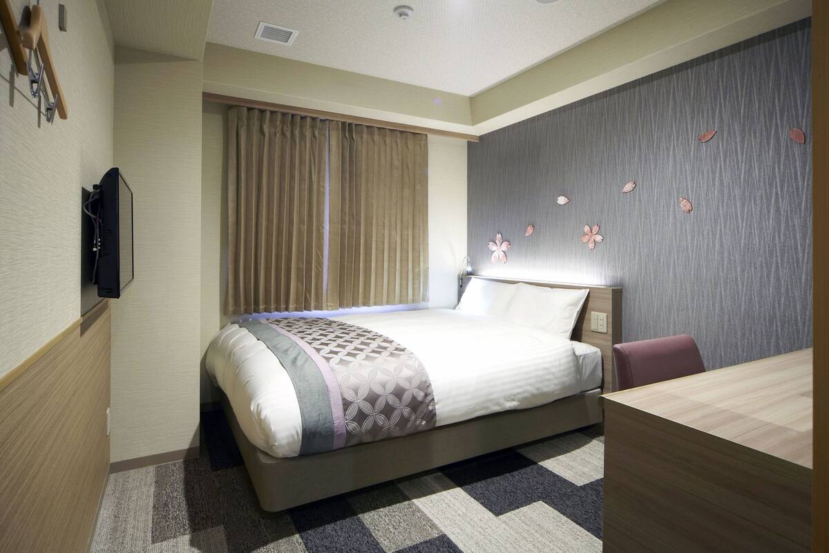 A hotel room with a bed, a desk, a chair, a TV, and a window with curtains.