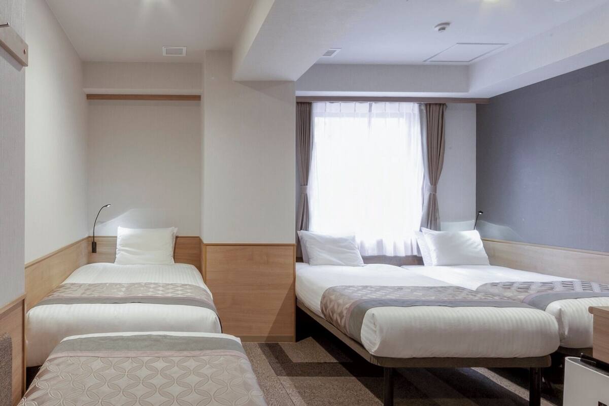 A hotel room with two beds, a desk, a TV, and a large window with curtains.