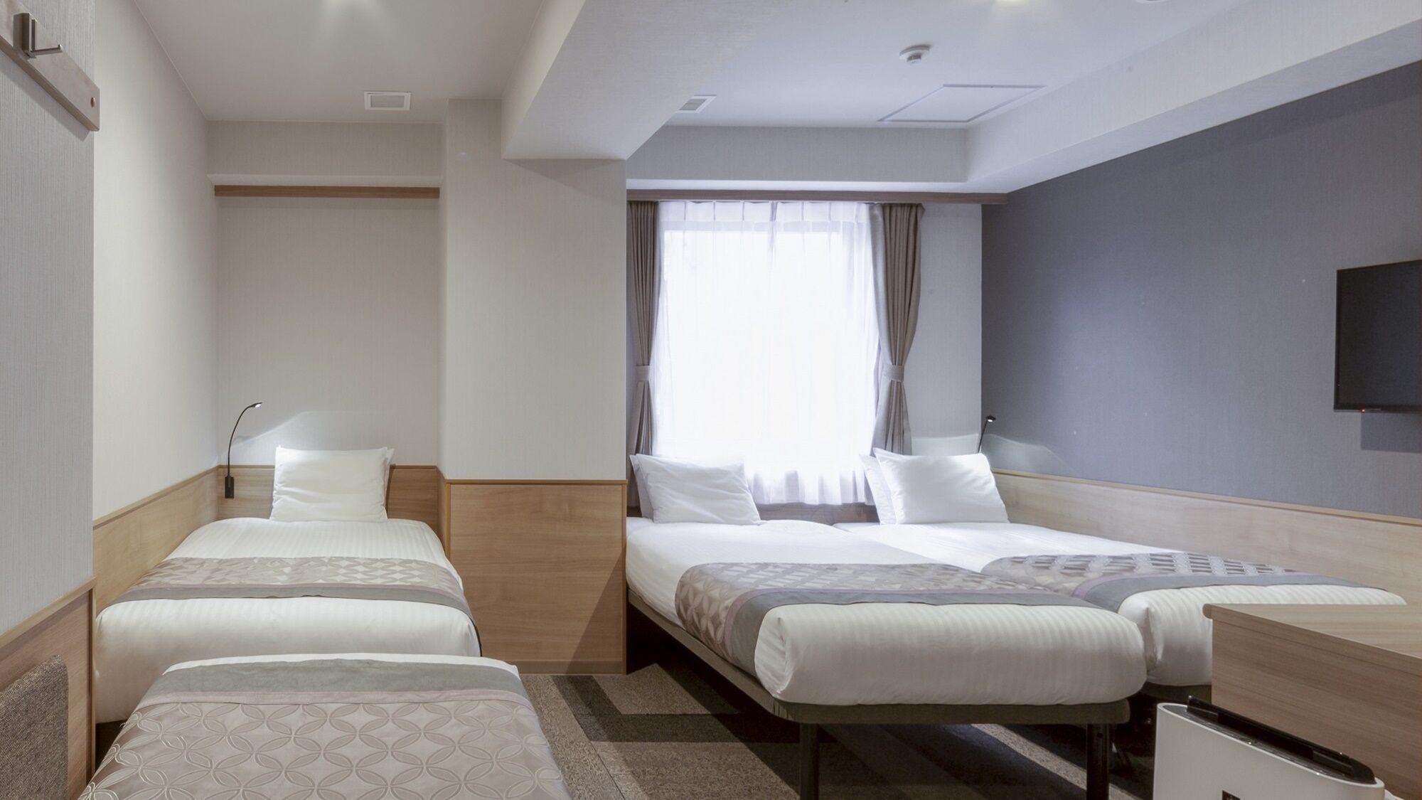 Une chambre d’hôtel avec deux lits simples, un bureau, une chaise, une télévision et une fenêtre avec des rideaux.