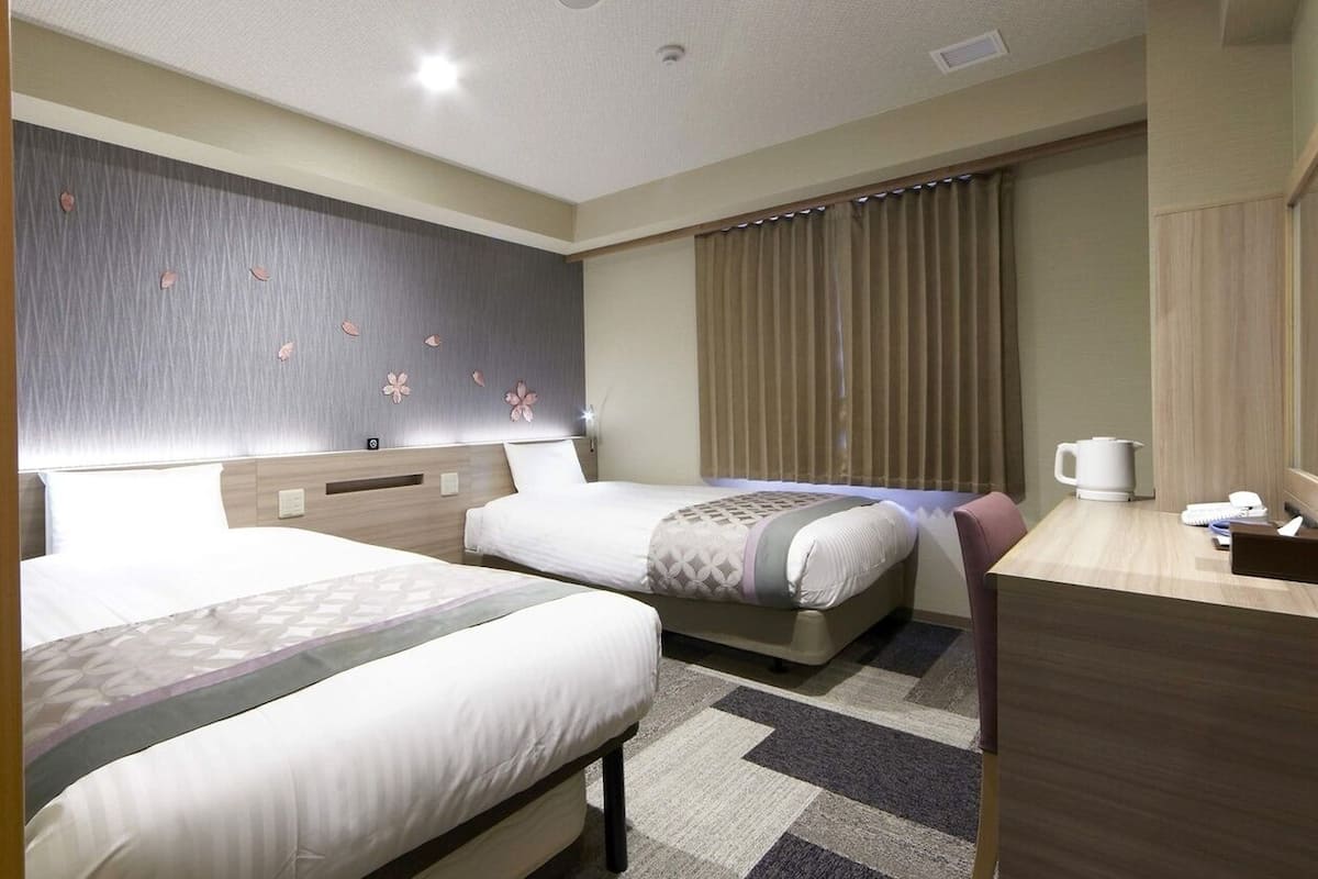 Une chambre d’hôtel avec deux lits, un bureau, une télévision et une fenêtre avec des rideaux.