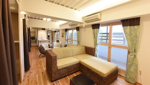 A spacious living area with a brown wicker sofa, a small table, and a view of the outdoors through large windows.