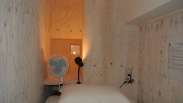Una habitación pequeña con paneles de madera, una cama, un ventilador y un espejo.