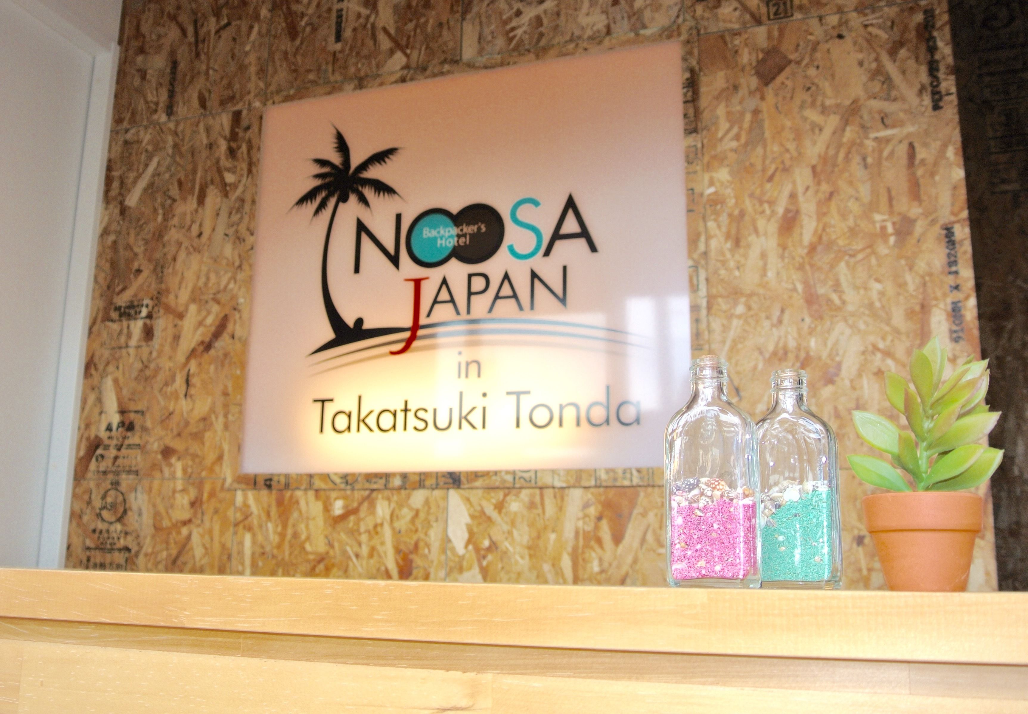 A sign for Noosa Japan in Takatsuki Tonda with three glass bottles and a potted plant.
