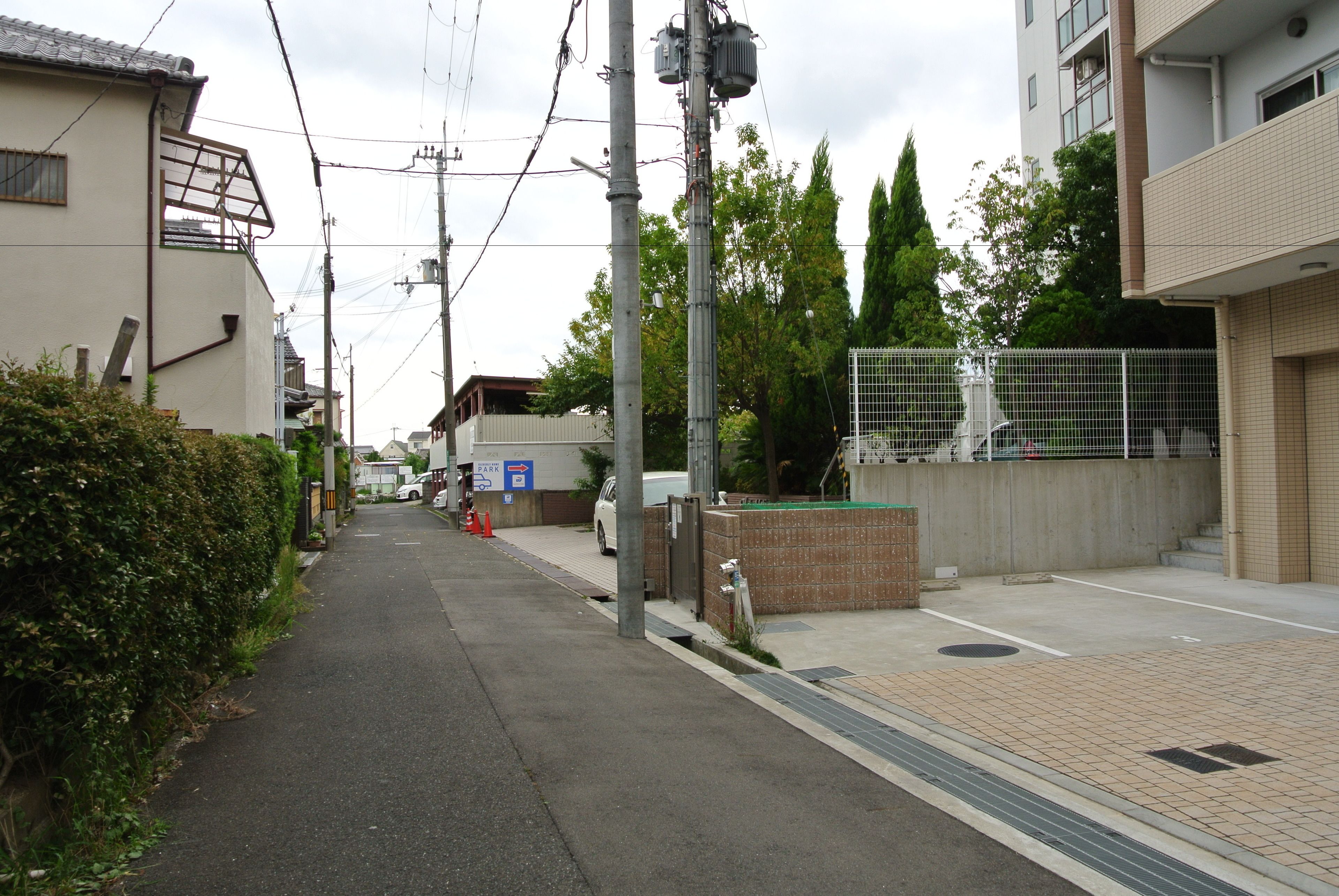 Une rue étroite en milieu urbain, bordée d’un trottoir, avec des voitures garées et des immeubles.