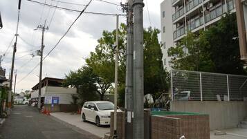 Una calle con un coche blanco estacionado al lado de la acera, un edificio de varios pisos y un área cercada con techo verde.
