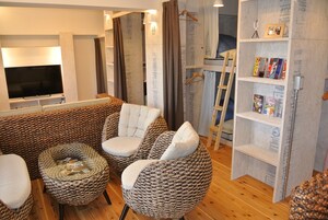 Una sala de estar con un televisor de pantalla plana grande, un sofá, dos sillones, una mesa de centro y una estantería con revistas.