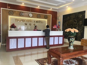 A reception desk with clocks indicating different time zones, a sign for Thanh Phu Hotel, and flags of various countries.