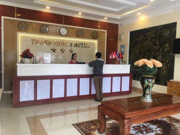 Una recepción con relojes mostrando diferentes husos horarios, un cartel para el Hotel Thanh Phu y banderas de varios países.