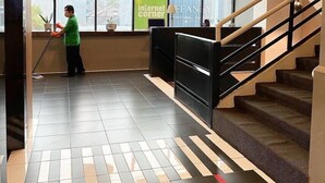 Un hall d’hôtel avec une grande fenêtre, un escalier et une personne qui nettoie.