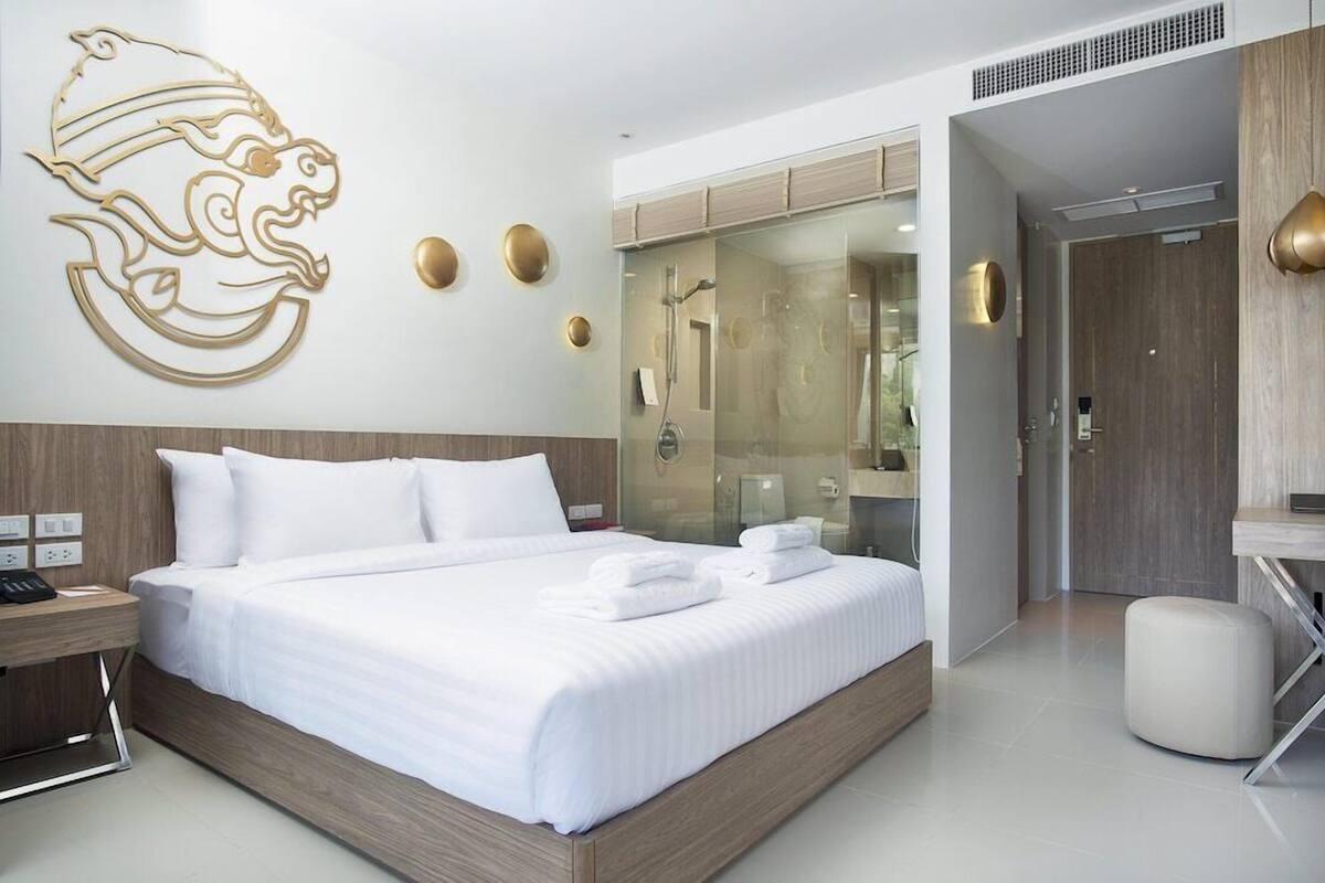 A modern hotel room with a large bed, a glass shower enclosure, and a wooden headboard.