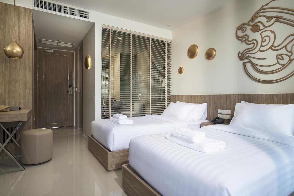 A modern hotel room with two beds, a wooden desk, a small stool, and a decorative wall piece.
