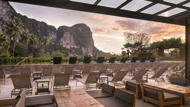An outdoor seating area with lounge chairs and tables, overlooking a mountainous landscape and a body of water. - Centara Life Phu Pano Krabi (Krabi)