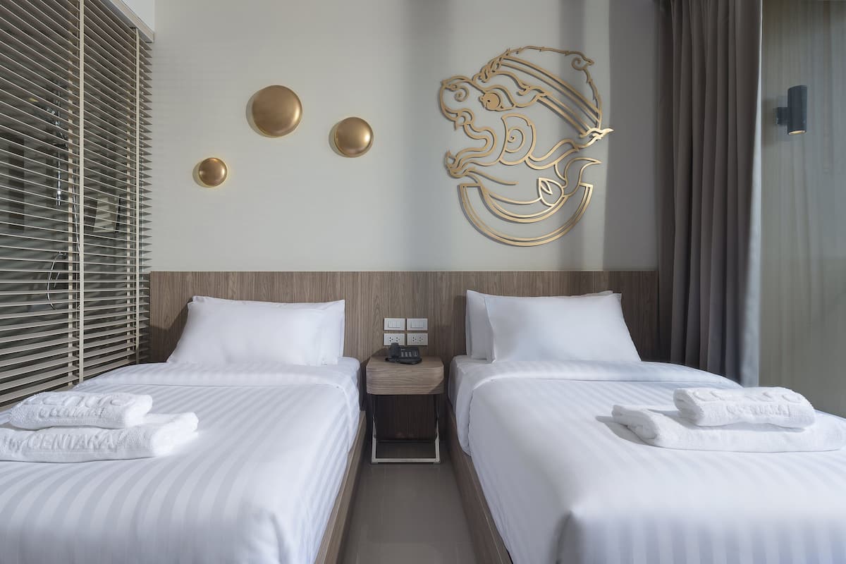 A hotel room with two beds, a wooden headboard, a wall-mounted light fixture, and a decorative wall piece.