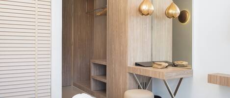 Habitación de hotel moderna con armario de madera, mesita de noche con una computadora portátil y un bolso, un cesto de basura y una cama con edredón blanco.