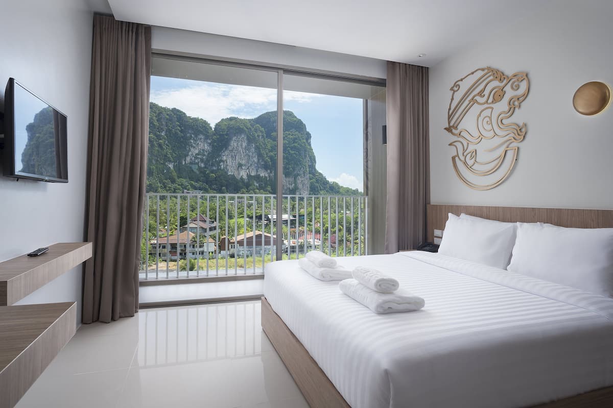 A hotel room with a large bed, a TV, a balcony with a view of mountains, and a decorative wall piece.