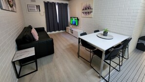 A compact living space with a sofa, a small dining table with chairs, a TV, and a potted plant. - Perth City Apartment Hotel (West Perth)