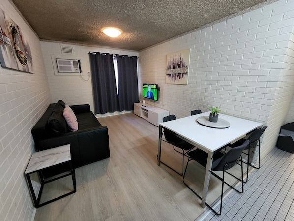 A compact living space with a sofa, a small dining table with chairs, a TV, and a potted plant.