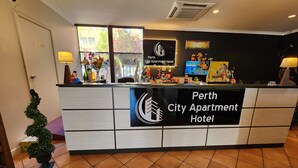 A reception desk at Perth City Apartment Hotel with a sign, a computer monitor, and a decorative plant. - Perth City Apartment Hotel (West Perth)