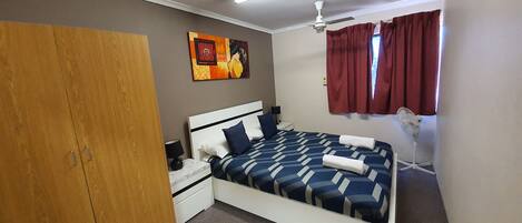 A bedroom with a bed, nightstand, wardrobe, ceiling fan, and artwork on the wall.