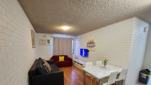 A compact living space with a black sofa, red sofa, and a dining table with chairs. - Perth City Apartment Hotel (West Perth)