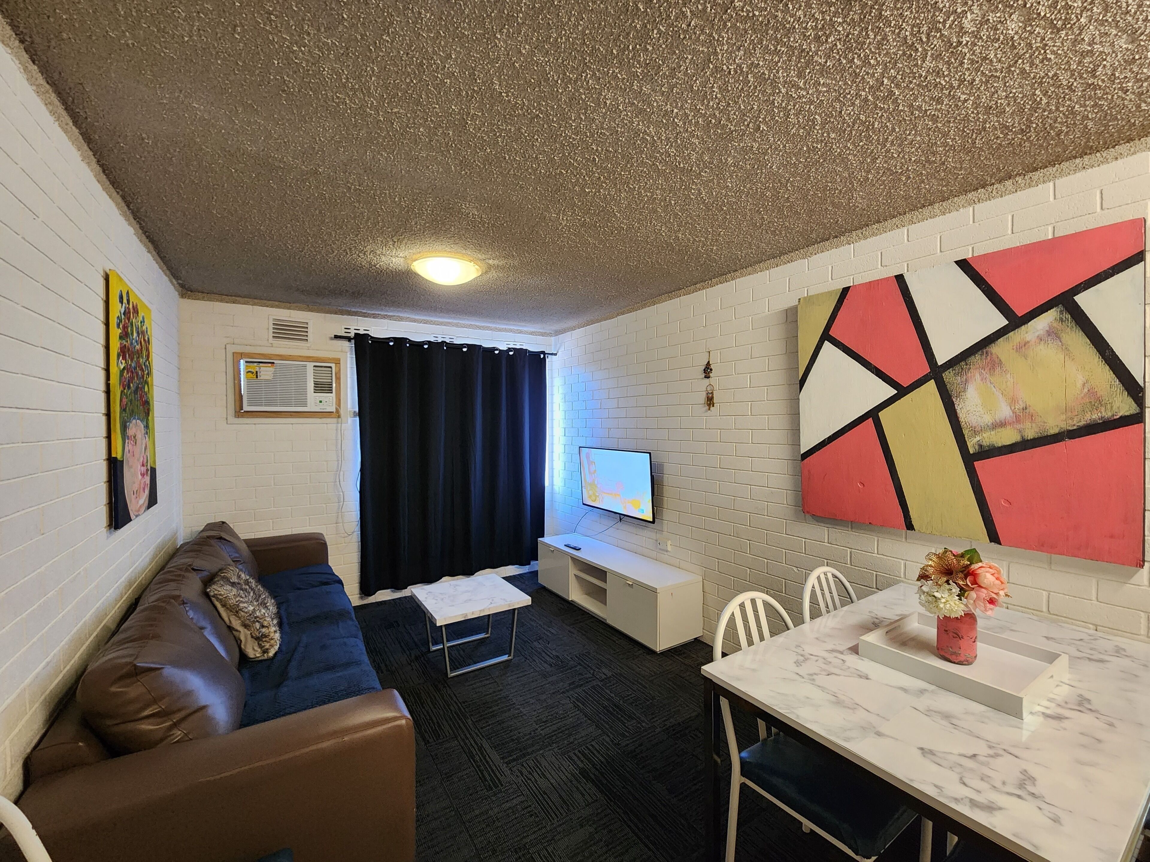 Ein modernes Wohnzimmer mit einer Couch, einem kleinen Tisch, einem Fernseher und einem Essbereich mit Stühlen.