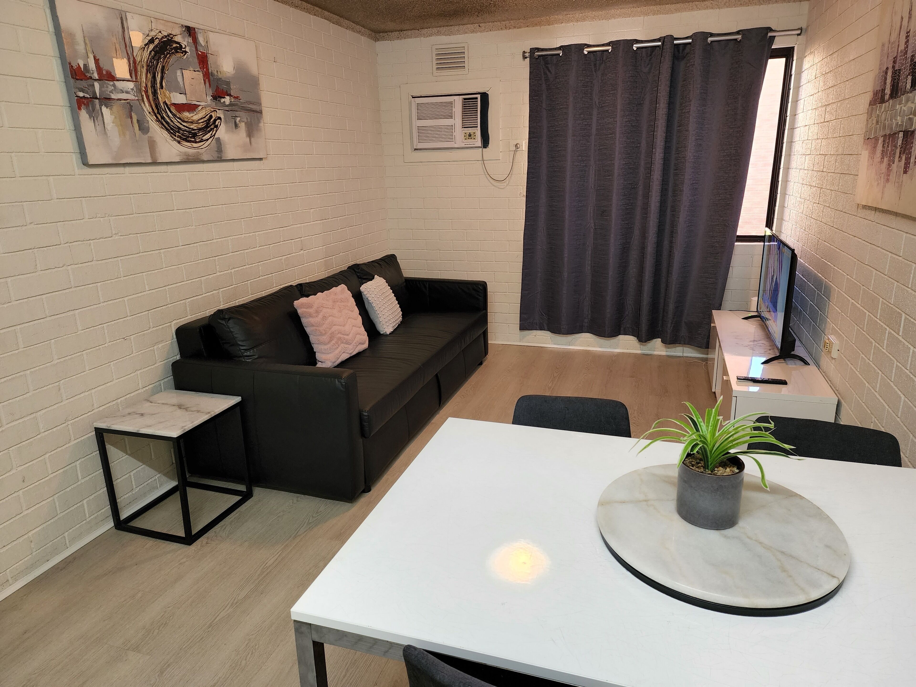Uma sala de estar moderna com um sofá de couro preto, uma mesa branca e uma planta em vaso.