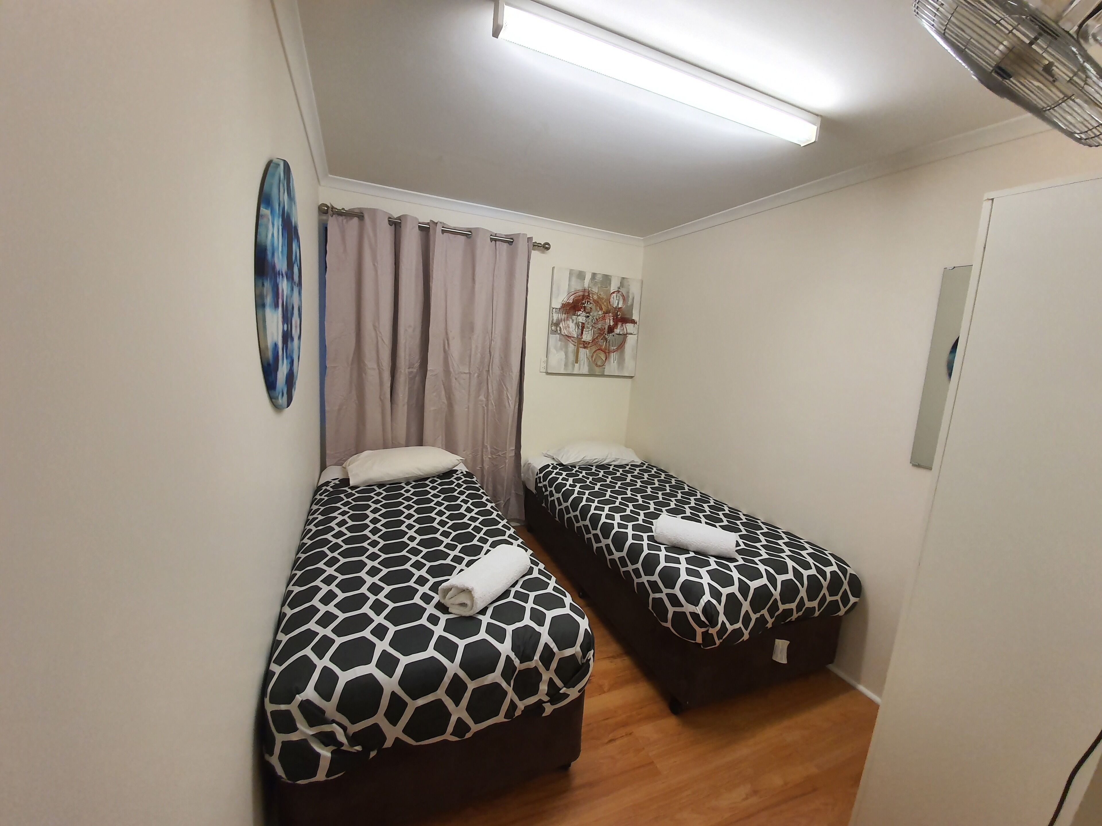 Una habitación pequeña y limpia, con dos camas, una lámpara en el techo y un cuadro en la pared.