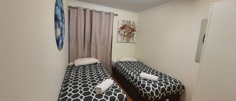 Una habitación pequeña y limpia, con dos camas, una lámpara en el techo y un cuadro en la pared.