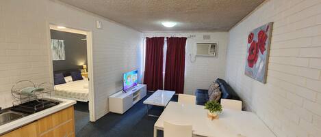 A compact hotel room with a kitchenette, a bed, a TV, a dining area, and a bathroom.