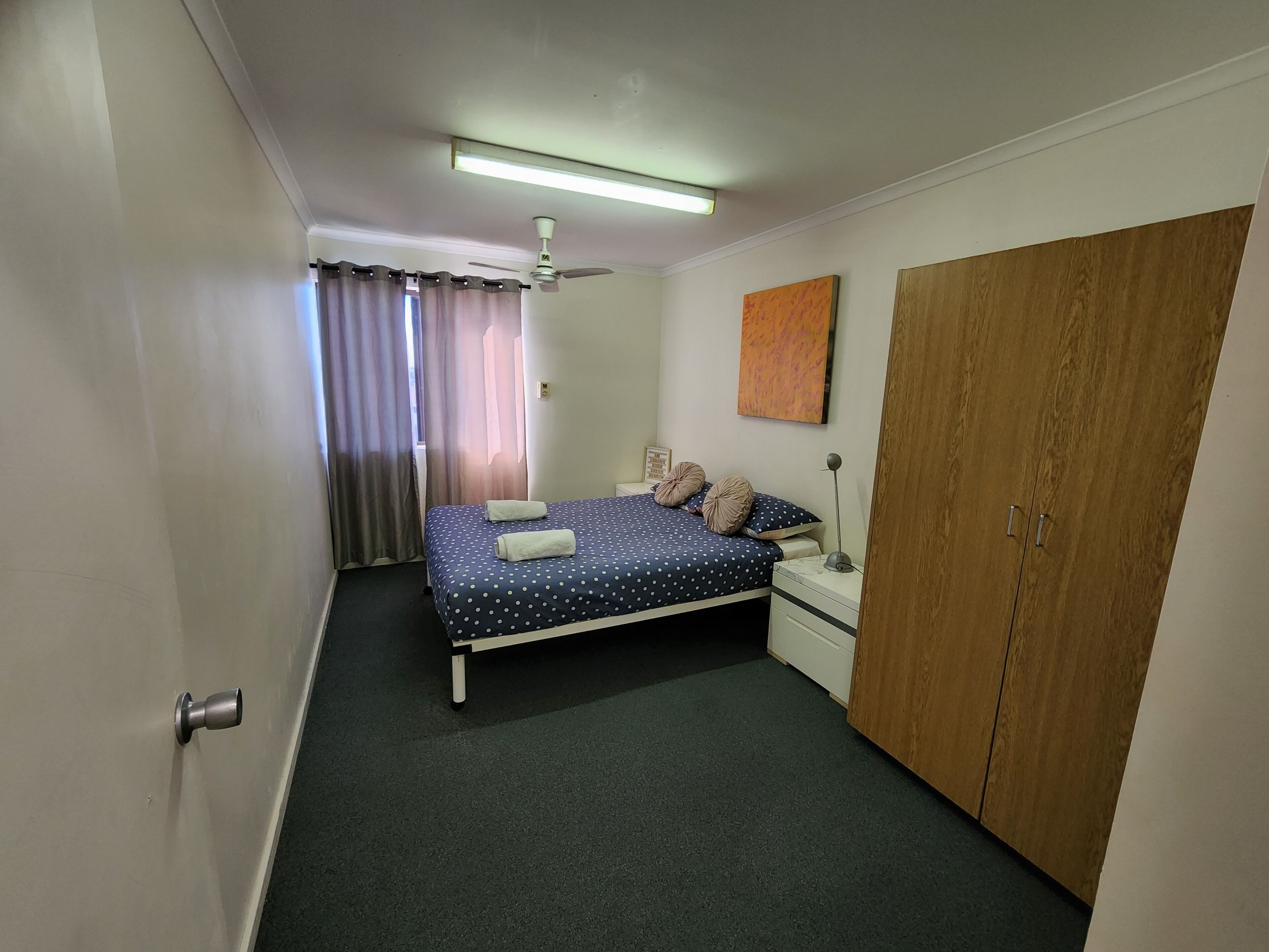 A bedroom with a bed, a nightstand, a wardrobe, a ceiling fan, and a window with curtains.