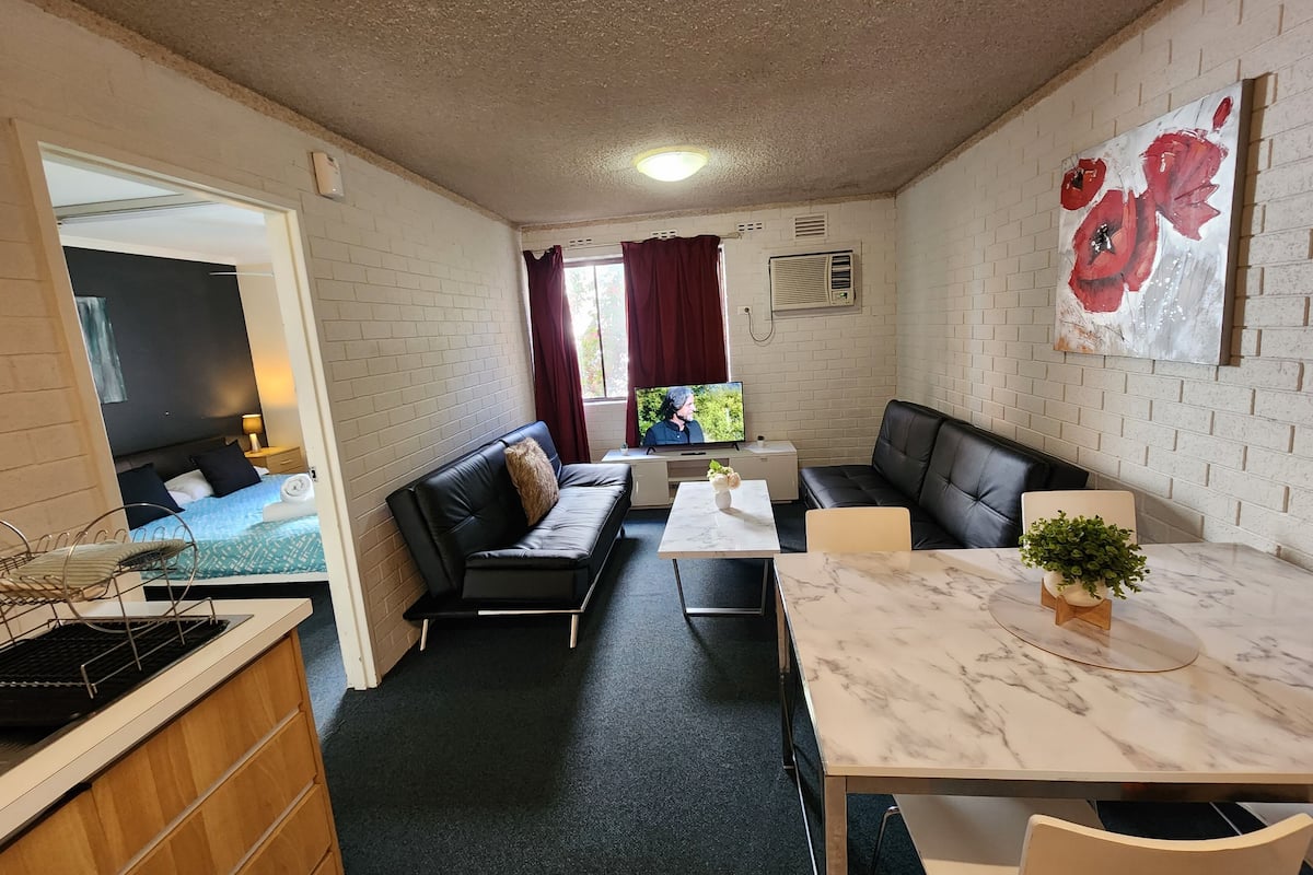 Ein kompakter Wohnbereich mit Küchenzeile, einer Couch, einem Esstisch und einem Fernseher.