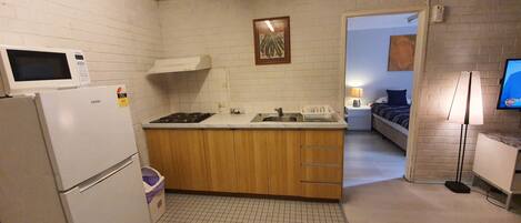 Una cocina compacta con refrigerador, microondas, estufa y lavamanos. En el fondo, se ve un pequeño comedor con una mesa y sillas.