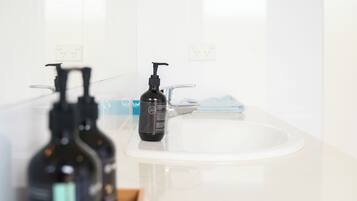 A bathroom with a white sink, a mirror, and two black bottles on a wooden tray.