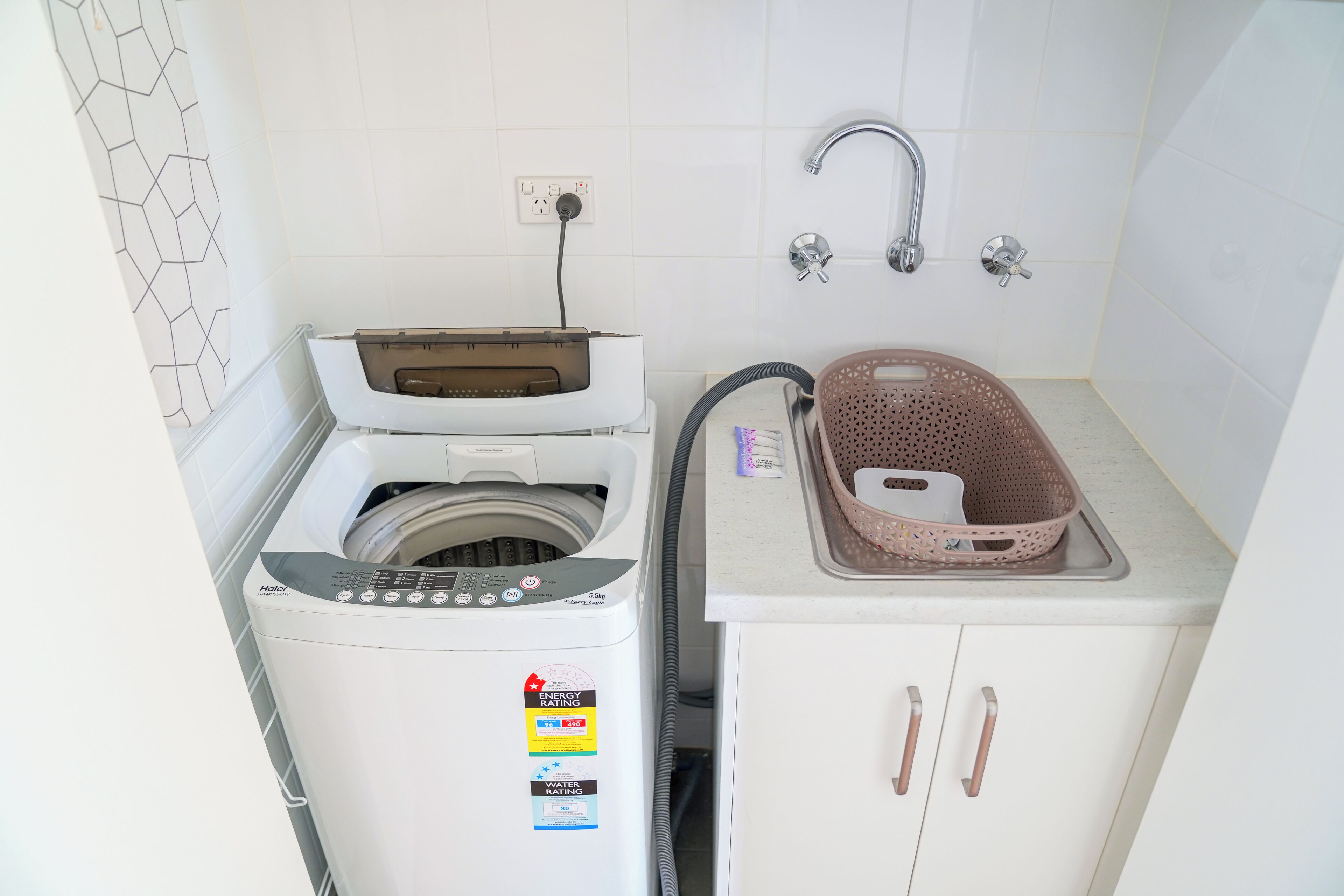 Un área de lavandería compacta con lavadora de carga frontal, un tendedero y un lavabo con cesto.