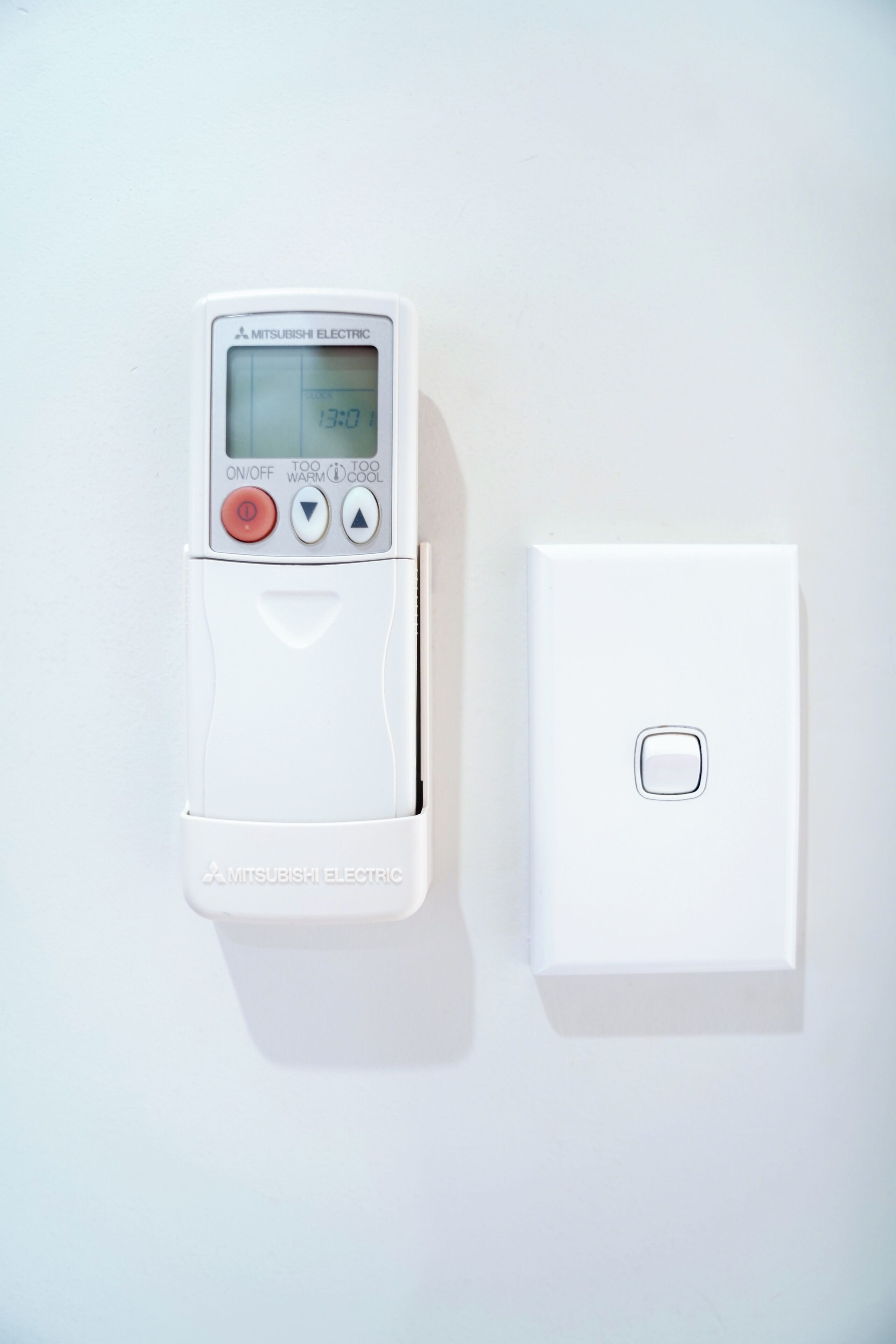 Un termostato blanco montado en la pared, con pantalla digital y botones de control, junto a un interruptor blanco sencillo.