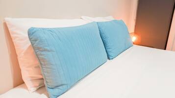A bed with white and blue pillows, a white mattress, and a bedside lamp.