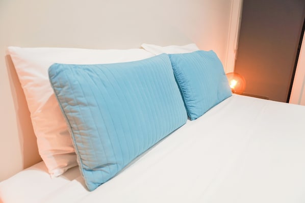 A bed with white and blue pillows, a white mattress, and a bedside lamp.