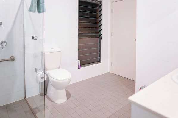 A bathroom with a toilet, a glass shower enclosure, and a window with blinds. - Villas on the Bay Kingscote (Kingscote)