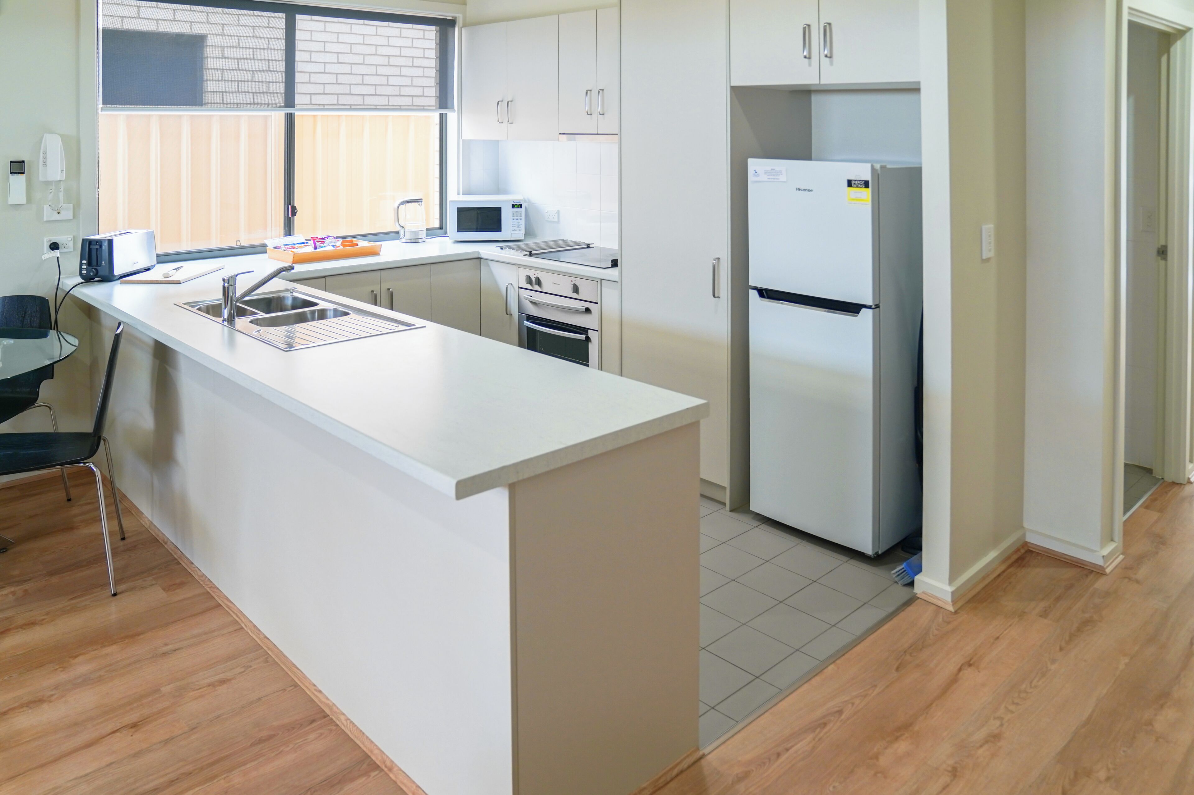 Una cocina moderna con una isla central, electrodomésticos de acero inoxidable y un ventanal con persianas.