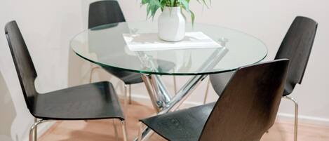A round glass table with four black chairs and a potted plant.