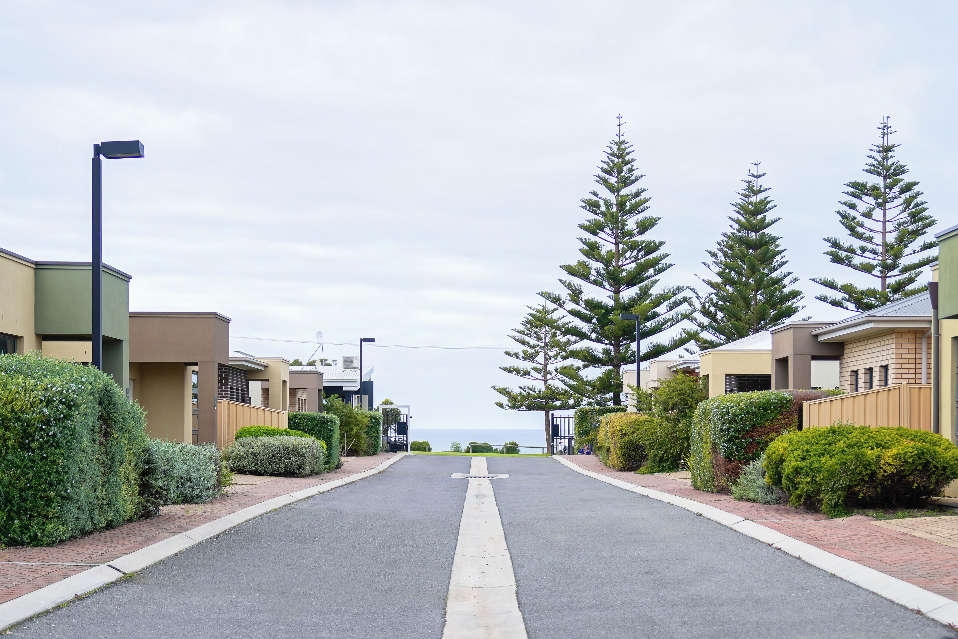 A residential street with modern houses, a clear sky, and a view of the ocean.